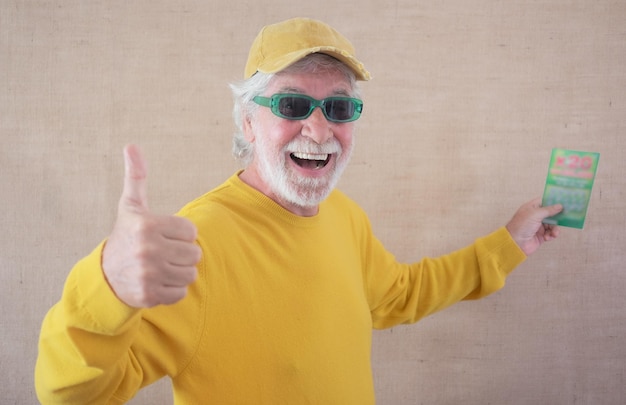Foto opgewonden senior man die een instant loterij wint en naar de camera kijkt met duim omhoog