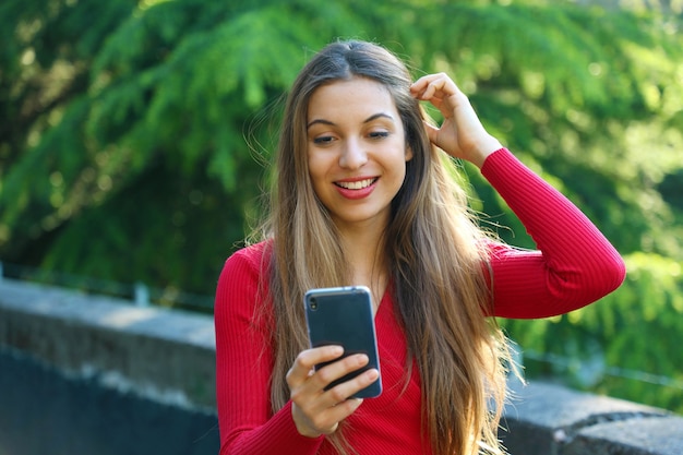 Opgewonden stedelijk meisje met behulp van nieuwe mobiele telefoon-app in stadspark