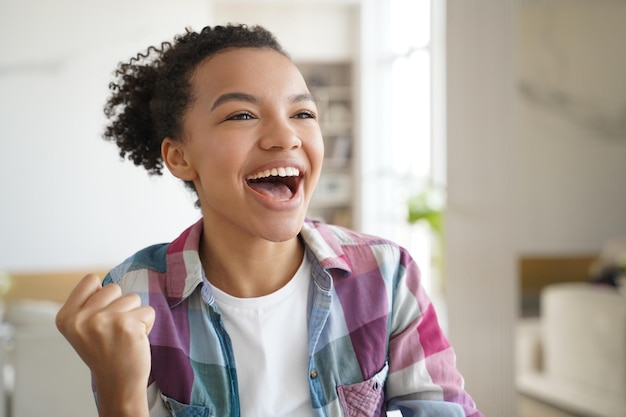 Opgewonden tienermeisje van gemengd ras maakt ja winnaar handgebaar viert succes persoonlijke prestatie