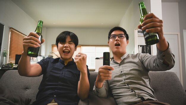 Opgewonden twee man bier drinken juichen voor voetbal op de bank thuis.