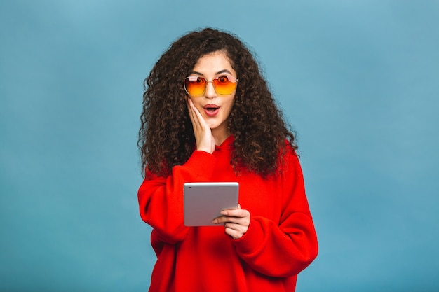 Opgewonden verbaasde jonge mooie vrouw met tablet-pc. Gelukkig meisje met behulp van tablet-computer, geïsoleerd op blauwe achtergrond.