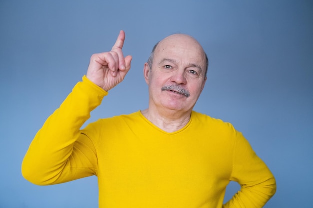 Opgewonden verbaasde man die met de vinger omhoog wijst op een blauwe studioachtergrond