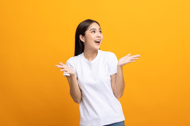 Opgewonden Verrast Aziatische vrouw met handen op geïsoleerde achtergrond. Blij geschokt gezicht vrouwelijk wow promotie reclameconcept. Vrolijke tienermeisje in wit overhemd staande in gele kamer.