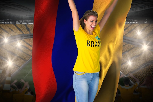 Opgewonden voetbalfan in brasil-t-shirt met colombia-vlag tegen enorm voetbalstadion met gele fans