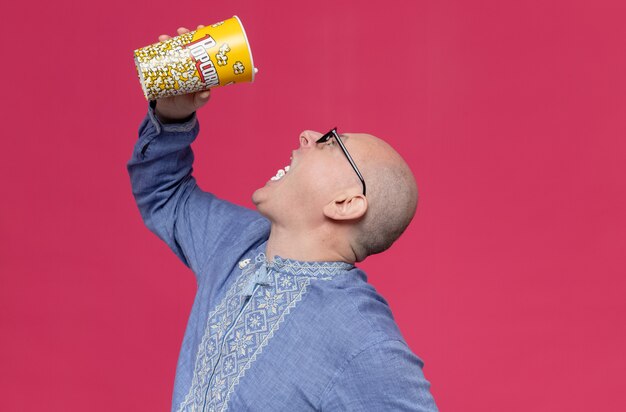 Opgewonden volwassen slavische man in blauw shirt met optische bril die popcorn eet