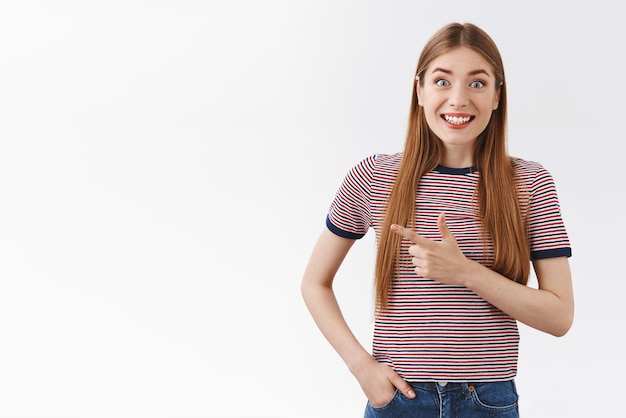 Opgewonden vrolijke en gelukkige jonge blanke vrouw met lang haar draagt een gestreept t-shirt glimlachend verbaasd en vrolijk wijzend naar links witte copyspace erg enthousiast bespreken geweldige kans