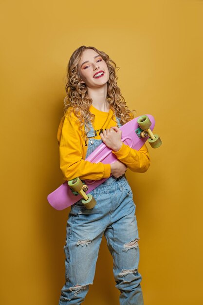 Opgewonden vrouw met skateboard op een felgele achtergrond Positieve emotie