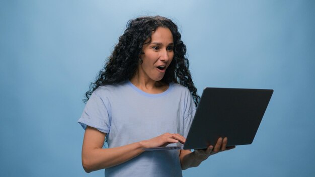 Opgewonden vrouw vrouwelijke Latino student meisje Spaanse gebruiker bedrijf winnen laptop online bereiken overwinning computer weddenschap goed resultaat kampioen efficiënte codering prestatie level up bonus op blauwe studio achtergrond