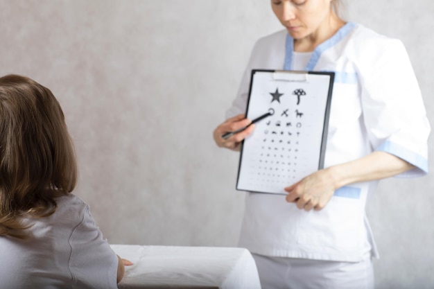 Ophthalmologist checks vision of 5 years old boy by means of eye chart for children.