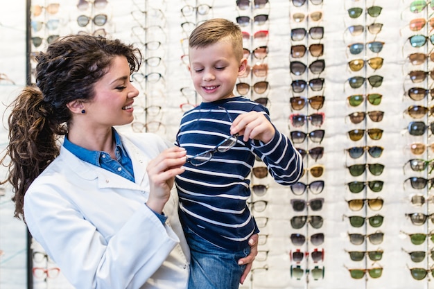 Ophthalmologist choosing eye frame for a little boy in optical store.