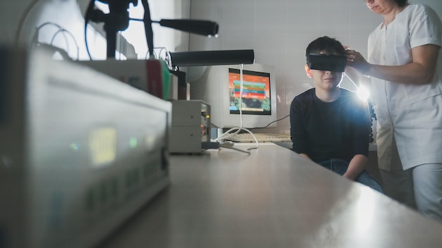 Il medico di oftalmologia controlla la visione del ragazzo con l'aiuto di occhiali per realtà virtuale stereovideo, grandangolo