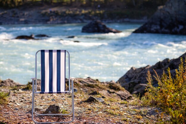 Opklapbare stoelen aan de oever van een bergrivier op een mooie, warme dag. Een rustige en stille plek om te ontspannen en na te denken. Uitrusting en rust van een toerist.