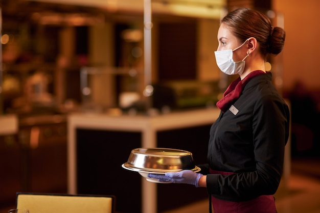 Foto oplettende serveerster die gezichtsmasker draagt tijdens het serveren van eten