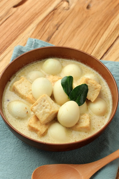 Opor tahu telur puyuh o curry indonesiano con tofu e uova di quaglia, servito su una ciotola marrone