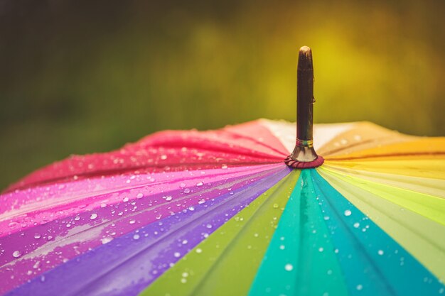 Oppervlak van regenboog paraplu met regendruppels erop.