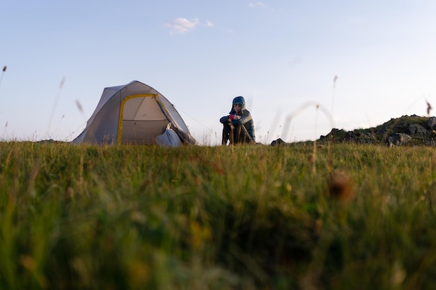 Oppervlakfoto van een vrouw die tijdens de zonsondergang bij een tent op het veld tegen de hemel zit
