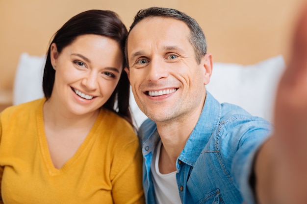 Oprechte glimlach. Positieve opgetogen man die een glimlach op zijn gezicht houdt en zijn vrouw omhelst