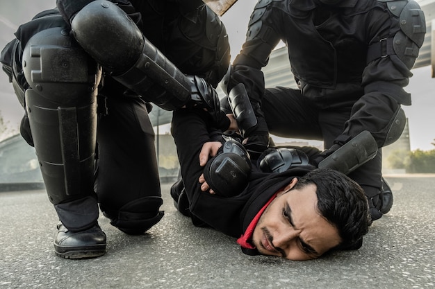 Oproerkracht in beschermende kleding drukt man uit het Midden-Oosten tegen de grond terwijl hij hem vasthoudt tijdens rally