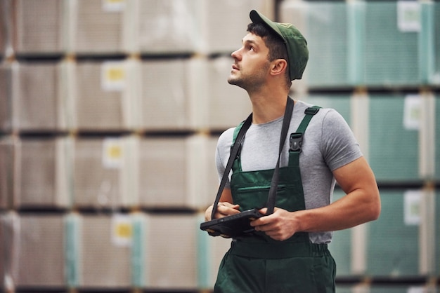 Opslagmedewerker in groen gekleurd uniform en notitieblok in handen controleert de productie.