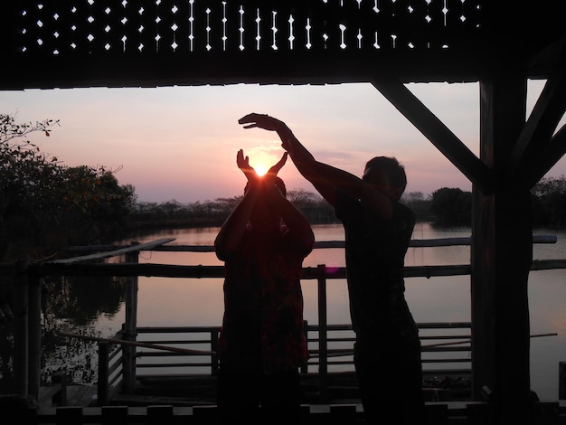 Photo optical illusion of friends holding sun against lake