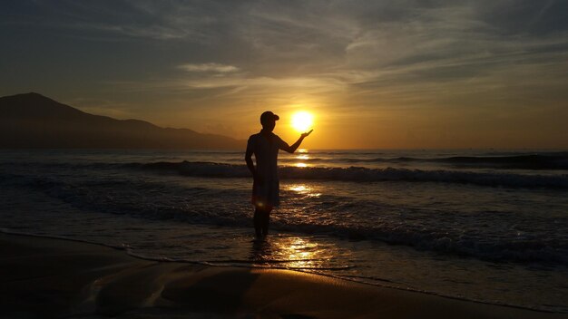 Optical illusion of man holding sun against sky during sunset