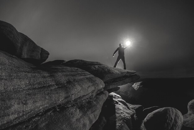 Photo optical illusion of silhouette man holding sun while standing on rock against sky