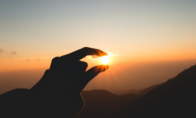 夕暮れ中に山の上で太陽を握っているシルエットの人物の光学錯覚