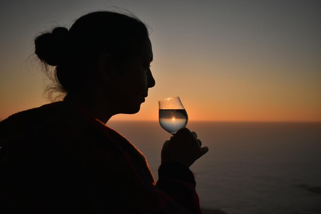 Foto illusione ottica di una silhouette di donna che tiene illuminate le stringhe di luci al tramonto