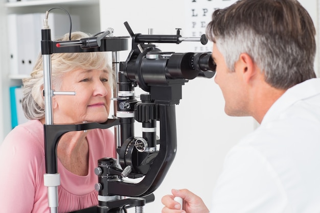 Photo optician examining senior female patient through slit lamp