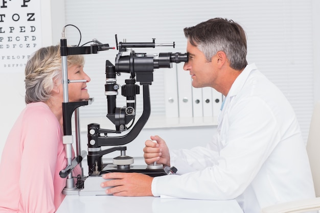 Optician examining senior patient through slit lamp