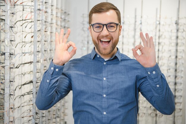 In optics shop portrait of male client holding and wearing
different spectacles choosing and trying on new glasses at optical
store man picking frame for vision correction closeup