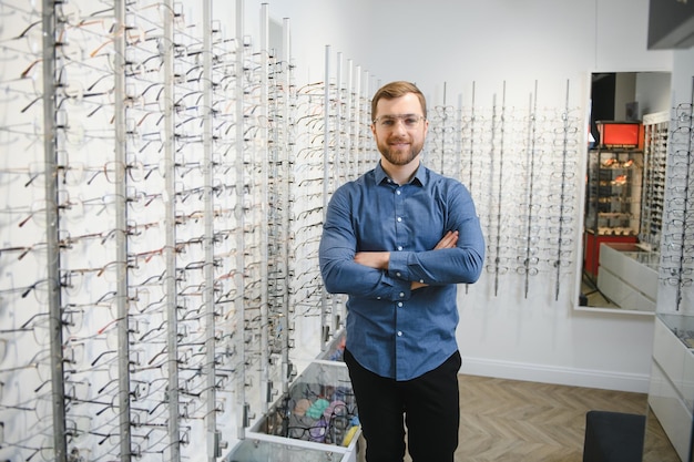 In optics shop portrait of male client holding and wearing\
different spectacles choosing and trying on new glasses at optical\
store man picking frame for vision correction closeup