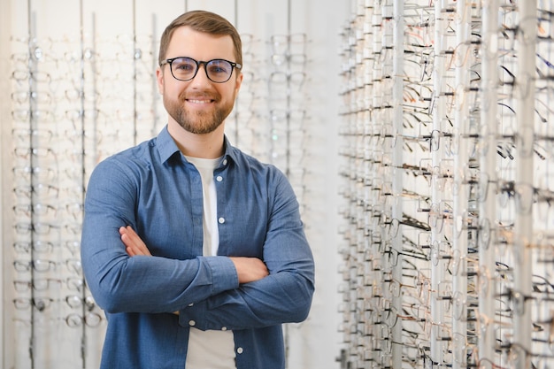 In Optics Shop Portrait of male client holding and wearing different spectacles choosing and trying on new glasses at optical store Man picking frame for vision correction closeup