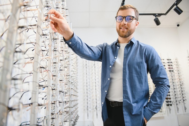 In Optics Shop Portrait of male client holding and wearing different spectacles choosing and trying on new glasses at optical store Man picking frame for vision correction closeup