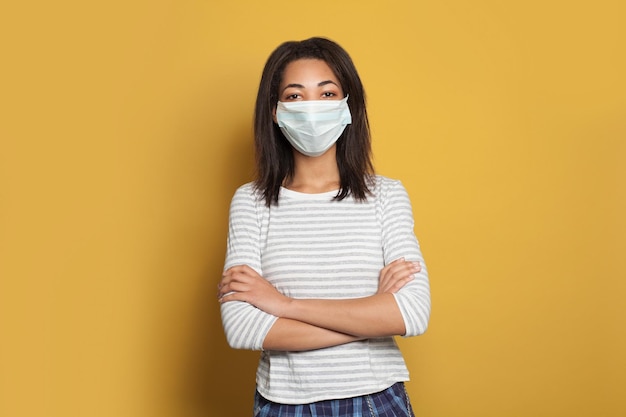 Optimistic African American woman in medical face mask on yellow background