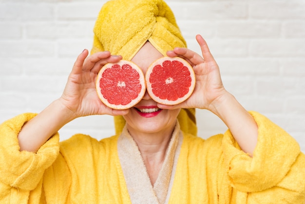 Optimistic aging lady closing eyes with grapefruit slices, cosmetic procedures