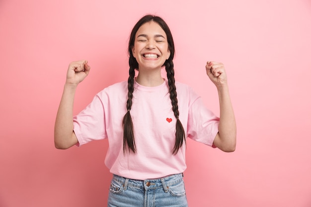 optimistic attractive girl with two braids smiling and rejoicing at front isolated over pink wall