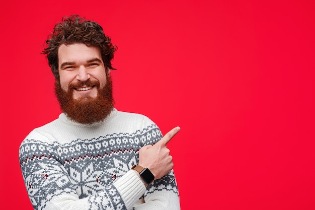 Photo optimistic bearded man smiling and pointing at empty space