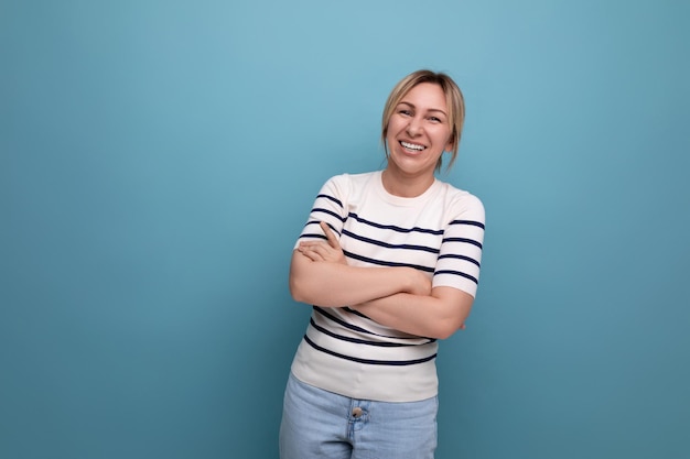 Optimistic happy blonde woman in casual outfit on blue studio background with copy space