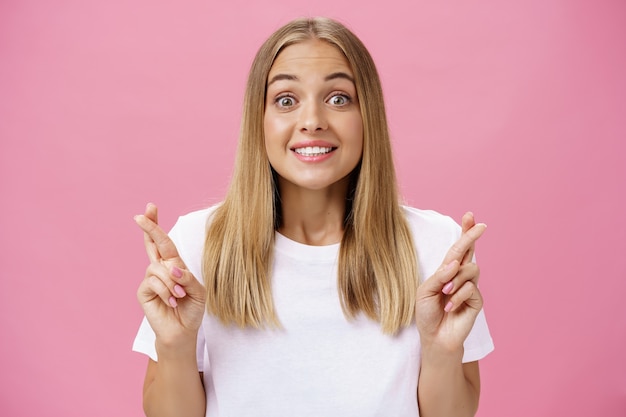 Ottimista promettente ragazza eccitata e capelli lisci biondi che vagano eccitati e felici alla telecamera che sorride contro il muro rosa