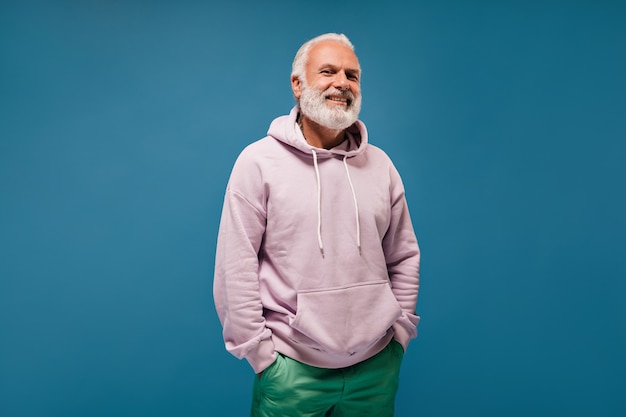 Optimistic man in green trousers and hoodie posing on blue wall