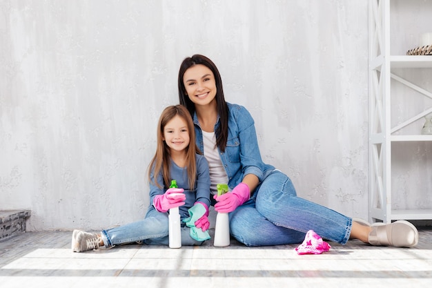 Optimistic mother and adorable girl resting on floor while holding sanitizer spray