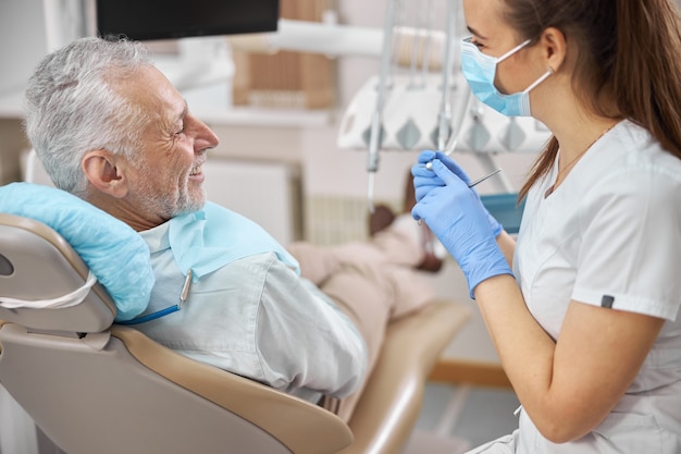 Optimistic senior citizen smiling at his joyful female dentist during a dental treatment