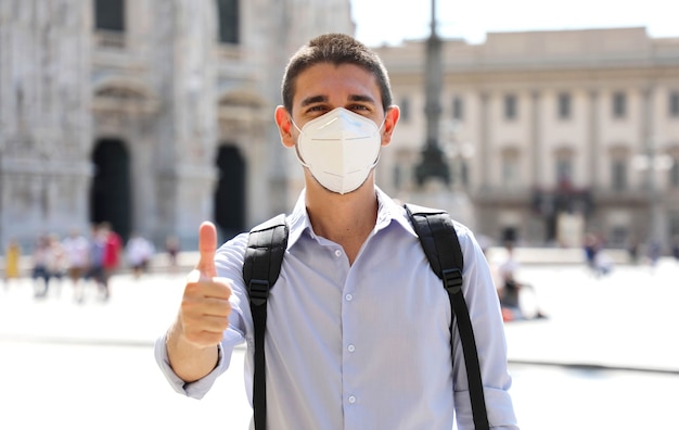 밀라노, 이탈리아에서 엄지 손가락을 보여주는 보호 마스크를 쓰고 낙관적 인 젊은 남자