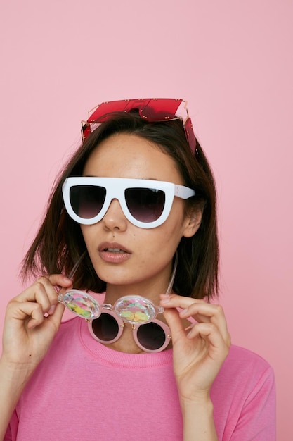 Optimistic young woman a lot of glasses on the face in a pink tshirt isolated background