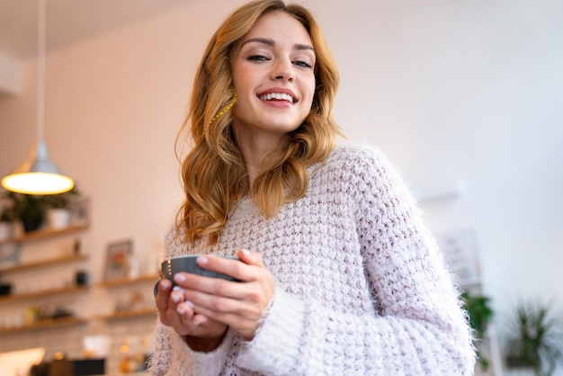 optimistisch blij gelukkige jonge blonde vrouw poseren in café binnenshuis koffie drinken.