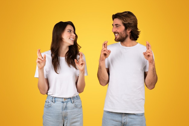 Optimistisch jong echtpaar in witte T-shirts die hun vingers kruisen voor geluk