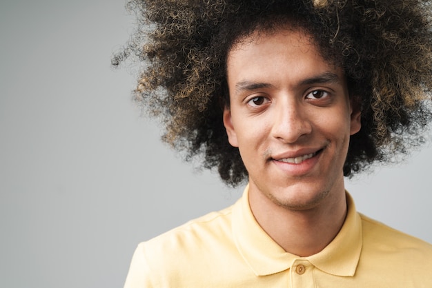 optimistische blanke man met afro kapsel kijken en glimlachen geïsoleerd over grijze muur