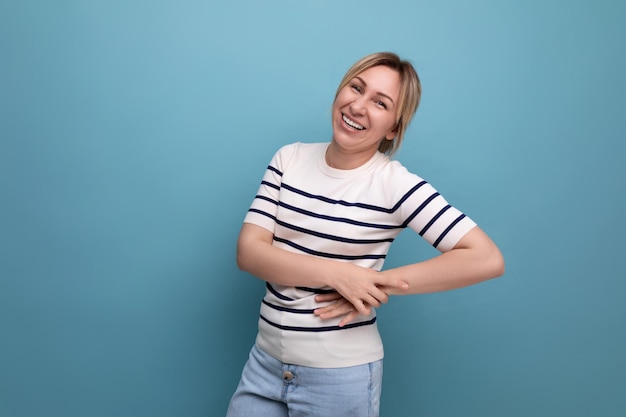 Optimistische gelukkige blonde vrouw in casual outfit op blauwe studioachtergrond met kopieerruimte