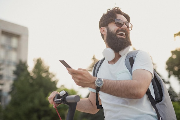 Optimistische hipster met smartphone rijdende scooter